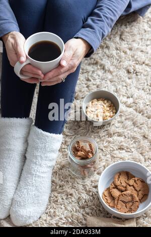 Frauen Hände halten Kaffeebecher mit Snack, Kekse, Nüsse und Zimt mit weichen gemütlichen Hintergrund Stockfoto