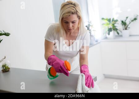 Frau in der Küche lächelt und wischt Staub mit einem Spray und einem Staubwedel, während sie ihr Haus putzt, Nahaufnahme Stockfoto