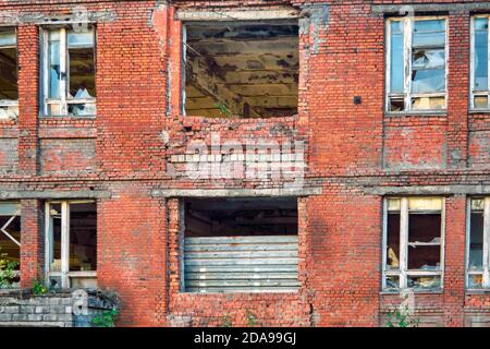 Ein Fragment eines alten verlassenen roten Ziegelgebäudes mit kaputten Fenstern. Stockfoto