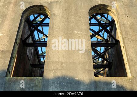 Die hohen, gewölbten Fenster und Metalldachbalken eines zerstörten Industriegebäudes, des alten Cornish Pumphouse in Waihi, Neuseeland Stockfoto