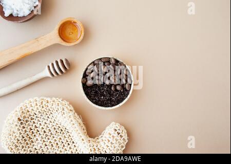 Kaffee-Peeling und Kaffeebohnen in Goldglas, Honig, kosmetisches Öl und Holzstab für Honig vor einem pastellbeigen Hintergrund, Hauskosmetik, Kosmetik Stockfoto