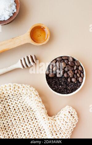 Kaffee-Peeling und Kaffeebohnen in Goldglas, Honig, kosmetisches Öl und Holzstab für Honig vor einem pastellbeigen Hintergrund, Hauskosmetik, Kosmetik Stockfoto