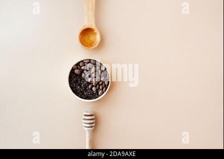 Kaffee Peeling und Kaffeebohnen in Gold-Glas, Holz Honigstock und kosmetisches Öl ordentlich auf pastellbeige Hintergrund organisiert, Home Kosmetik, Kosmetik l Stockfoto