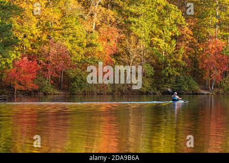 Kajakfahrer gleiten bei Sonnenuntergang am Stone Mountain Lake im Stone Mountain Park in der Nähe von Atlanta, Georgia, vorbei an lebendiger Herbstfärbung. (USA) Stockfoto