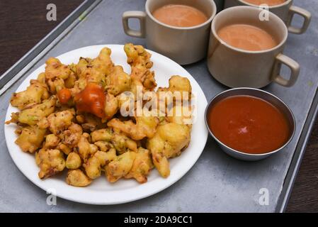 Zwiebel Pakora oder Pakoda oder Gemüse fritters mit Tomatensauce und heißem Tee, indische Street Food Snack Jaipur, Rajasthan Indien. Frittierte Fast Food Stockfoto