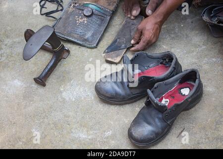 Indische lokale Schuster Reparatur Schuhe neben der Straße von Hand mit Werkzeugen in traditioneller Weise. Natürliche Schuss Darstellung der täglichen Arbeit eines regelmäßigen Schuster. Stockfoto