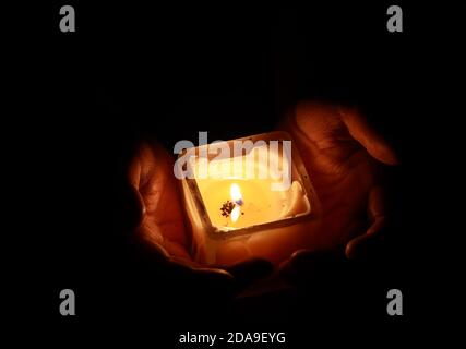 Hände halten eine schöne quadratische Kerze mit glühender Flamme während der Festlichkeiten von diwali oder kalipuja in indien. Foto mit dunklem b aufgenommen Stockfoto