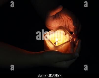 Hände halten eine schöne quadratische Kerze mit glühender Flamme während der Festlichkeiten von diwali oder kalipuja in indien. Foto mit dunklem b aufgenommen Stockfoto