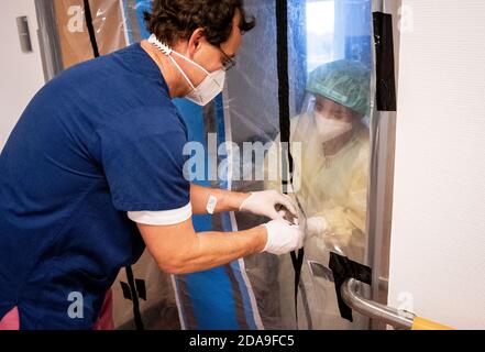 Berlin, Deutschland. November 2020. In den frühen Morgenstunden nimmt Krankenschwester Tillmann von seinem Kollegen in Schutzkleidung mit Mund-Nase-Abdeckung, Gesichtsmaske, Kittel und Haube Blutproben durch die Luftschleuse in das Patientenzimmer der Covid-19-Station des Bethel-Krankenhauses Berlin. Die Covid-Station behandelt Patienten, die positiv auf Corona getestet wurden und keine Atmung benötigen oder einen starken Verdacht auf Corona zeigen. Quelle: Kay Nietfeld/dpa/Alamy Live News Stockfoto