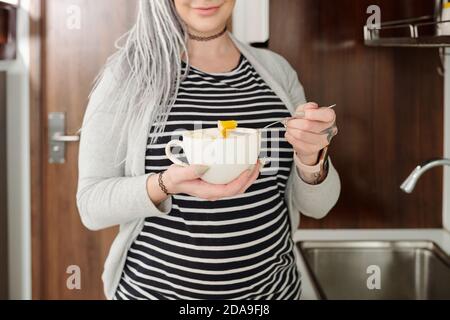 Zugeschnittenes Bild von lächelnden jungen schwangeren Frau mit Schüssel Obstsalat als Snack Stockfoto