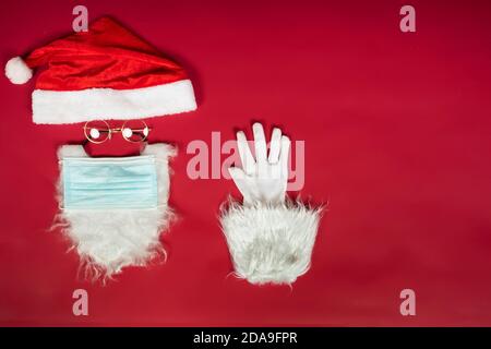 Weihnachtsmann Kopf mit OP-Maske, Hut, weißem Bart und Handschuhe mit Kopierraum auf rotem Hintergrund. Stockfoto