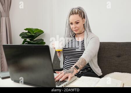 Schwangere stilvolle junge schwangere Frau trinken koffeinfreien Kaffee und Und E-Mails auf dem Laptop abrufen Stockfoto