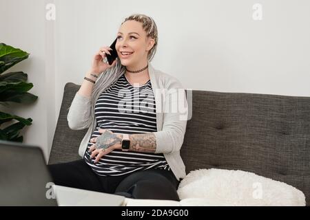Glückliche schwangere junge Frau im Gespräch am Telefon mit Verwandten oder Freund und berühren ihren Bauch Stockfoto