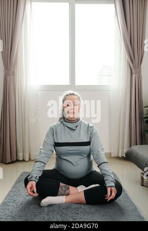 Beautoful junge Frau mit Dreadlocks sitzen auf dem Boden in Wohnzimmer und meditieren in Lotusposition Stockfoto