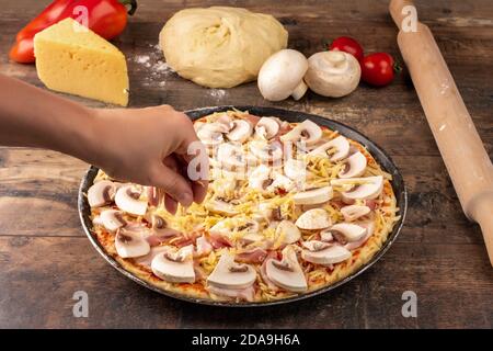 Frische original italienische rohe Pizza, Vorbereitung mit Pilzen. Prozess der Herstellung von Pizza. Weibliche Hände gerieben Käse auf Pizza, Pizza Kochen in einem Stockfoto