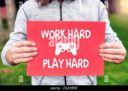 Männlich Teenager Gamer hält ein Banner mit Arbeit hart spielen hart Zitat mit einem Gamepad Symbol. Motivation oder Inspiration für Gamer. Stockfoto