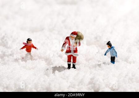 Miniatur Vater Weihnachten oder Weihnachtsmann mit einem Sack Geschenke Wandern durch dicken weißen Winterschnee begleitet von einem Junge Mädchen und Junge mit Co Stockfoto