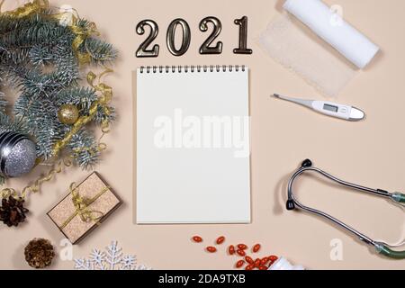 Neujahrskarte zu medizinischen Themen: Zahlen 2021, Phonendoskop, Tabletten, Thermometer und Verband mit Fichtenzweig auf beigem Hintergrund. Stockfoto
