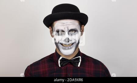 Ein beängstigender Clown schaut auf die Kamera und lacht schrecklich. Unheimliche Grimassen eines Clowns, der die Kamera anschaut. Stockfoto