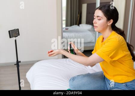 Vlogging. Eine junge hübsche weibliche Vlogger Streaming Live-Video auf Smartphone und testen an sich ein neues Kosmetik. Seitenansicht. Inneneinrichtung. Stockfoto