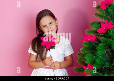 Nahaufnahme Porträt eines schönen Mädchen in einem weißen Kleid mit einer Blume neben dem Weihnachtsbaum, auf einem rosa Hintergrund Stockfoto