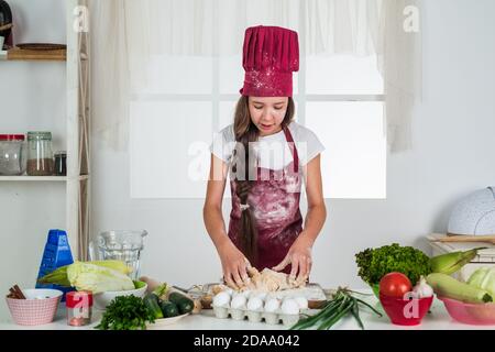 Happy Kind tragen Koch Uniform. Chef Mädchen in Hut und Schürze. Kind Kochen Lebensmittel in der Küche. Die Wahl einer Karriere. Kleine Helfer kneten Teig. Kulinarische und Küche. Glückliche Kindheit. Koch bereit zu kochen. Stockfoto