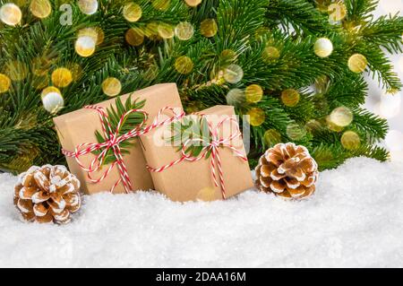 Zwei handgefertigte Weihnachtsgeschenke ohne Plastik unter Tannenbaum. Geschenke eingewickelt in Bastelpapier und Seil Bogen stehen im Schnee mit Kiefernästen und Bokeh Stockfoto