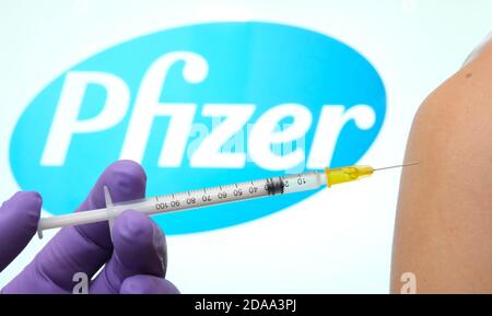 Pfizer BioNTech Covid-19 Impfstoffkonzept. Hand hält eine Spritze gegen die Frau Schulter, mit verschwommenem Pfizer-Logo auf der Rückseite. Stockfoto