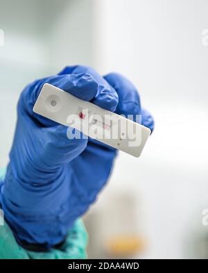 Hand einer Krankenschwester mit persönlicher Schutzausrüstung, die einen schnellen Coronavirus-Test mit negativem Ergebnis hält. Stockfoto