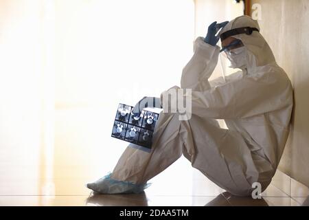 Müde Arzt in schützenden Anti-Pest Overalls siting im Korridor Klinik Stockfoto