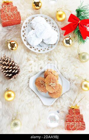 Melomakarona und kourabiedes, traditionelle griechische Weihnachtsdesserts und Weihnachtsschmuck Auf Schaffellteppich Stockfoto