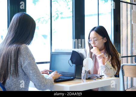 Zwei Schülerinnen mit Gesichtsmasken, die in einem Restaurant an ihren Computern arbeiten. Neue Normalität in Restaurants. Coronavirus-Pandemie. Stockfoto