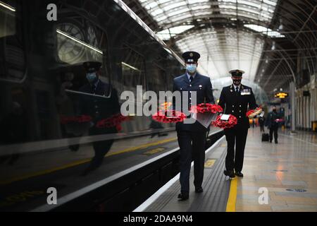 Militärangehörige tragen Mohnkränze am Bahnhof Paddington in London für „Mohnblumen nach Paddington“. Die Great Western Railway (GWR) und die Veterans Charity transportieren Gedenkkränze aus ganz Großbritannien mit dem GWR-Zug nach London Paddington, wo die Kränze um das Kriegsdenkmal des Bahnhofs gelegt werden, um zwei Minuten lang an die Kriegtot am Waffenstillstandstag zu erinnern. Stockfoto