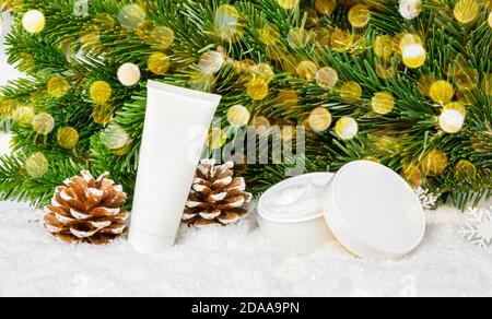 Winter Hautpflege Kosmetik-Produkte im Schnee unter Weihnachtsbaum mit Tannenzapfen und Bokeh Lichter. Gesichts-Creme-Glas und Handcreme oder Körperlotion Tube Stockfoto