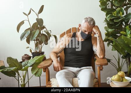 Verärgert mittleren Alters kaukasischen Mann trägt Schutzmaske während Coronavirus-Pandemie auf dem Balkon oder der Terrasse seines Wohnung Stockfoto