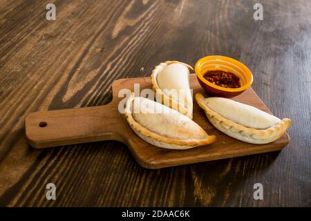 Traditionelle gebackene argentinische Empanadas herzhaftes Gebäck mit Fleischbeef Füllung oder Gemüse vor Holzhintergrund und würziger Sauce. Lateinamerikanisch Stockfoto