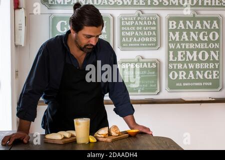 Ein charmanter Koch präsentiert neue Gerichte Kreation in einem kleinen Restaurant in Lissabon. Fröhlicher Restaurantbesitzer, der die neuen Empanada Teller und das Portug vorführt Stockfoto