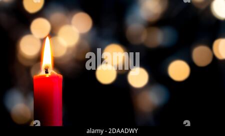 Eine rote Kerze brennt im Vordergrund vor einem bunten Bokeh Hintergrund. Konzept der Weihnachtsstimmung Stockfoto
