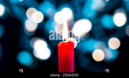 Eine rote Kerze brennt im Vordergrund vor einem bunten Bokeh Hintergrund. Konzept der Weihnachtsstimmung Stockfoto