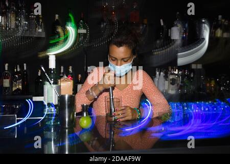 lateinamerikanische Kellnerin mit Gesichtsmaske in einer Nachtclub-Bar. Bewegungsunschärfe. Leerzeichen für Text. Stockfoto