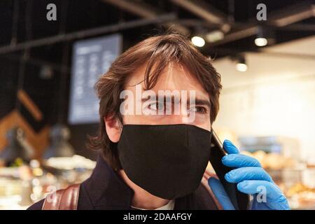 Kunde mit Gesichtsmaske wegen Covid-19 Pandemie mit Smartphone Beim Einkaufen Stockfoto