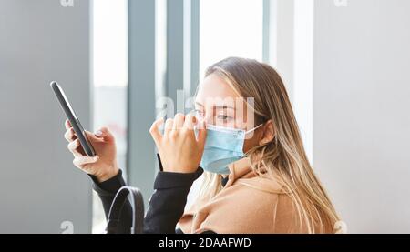 Frau mit Maske wegen Covid-19 schaut besorgt auf Smartphone Mit Coronavirus Warnung App Stockfoto