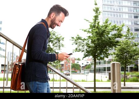 Seitenportrait mit lächelndem reifen Mann, der die Treppe hinunter geht und SMS auf dem Handy liest. Stockfoto