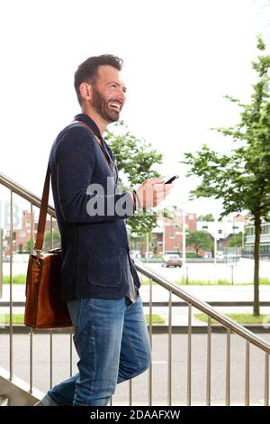 Seitenportrait mit lächelndem reifen Mann, der mit dem Handy die Treppe hinuntergeht. Stockfoto