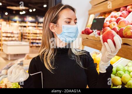 Kunde mit Gesichtsmaske wegen Covid-19 Pandemie beim Einkaufen Für Obst mit einem Apfel Stockfoto