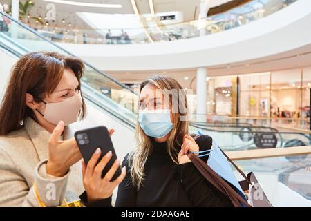 Zwei Freunde mit Smartphone und Gesichtsmaske wegen Covid-19 Beim Einkaufen Stockfoto