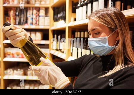 Weibliche Kundin mit Gesichtsmaske und Handschuhen, die Wein kaufen Der Supermarkt Stockfoto