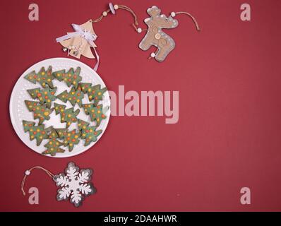 Weihnachts-Lebkuchenplatte in Form von Weihnachtsbäumen mit Weihnachtsspielzeug auf rotem Hintergrund.Nahaufnahme, Kopierraum. Horizontale Ausrichtung Stockfoto