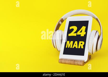 März. Tag 24 des Monats, Kalenderdatum. Elegante Kopfhörer und modernes Tablet auf gelbem Hintergrund. Leerzeichen für Text. Konzept Bildung, Technologie, Stockfoto