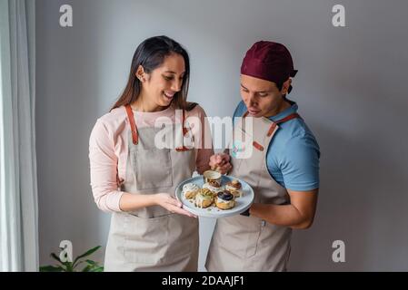 Hispanische Paar bereitet Zimtrollen von zu Hause auf einem grauen Wandhintergrund Stockfoto